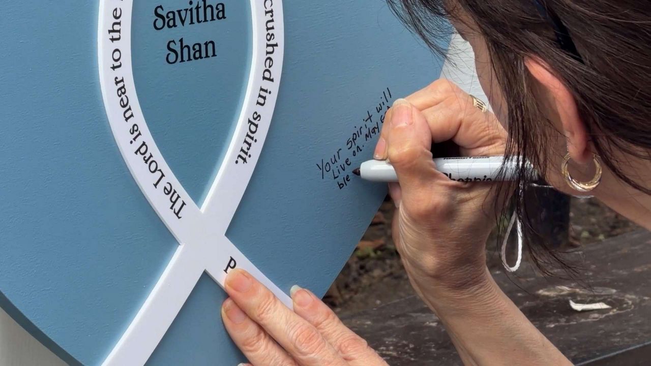 A person writes a message on the blue heart-cross for 21-year-old Savitha Shan, who was one of three people who died in a shooting outside of an Austin bar on Sunday, March 1, 2026. (Spectrum News 1/Barbara Fox)