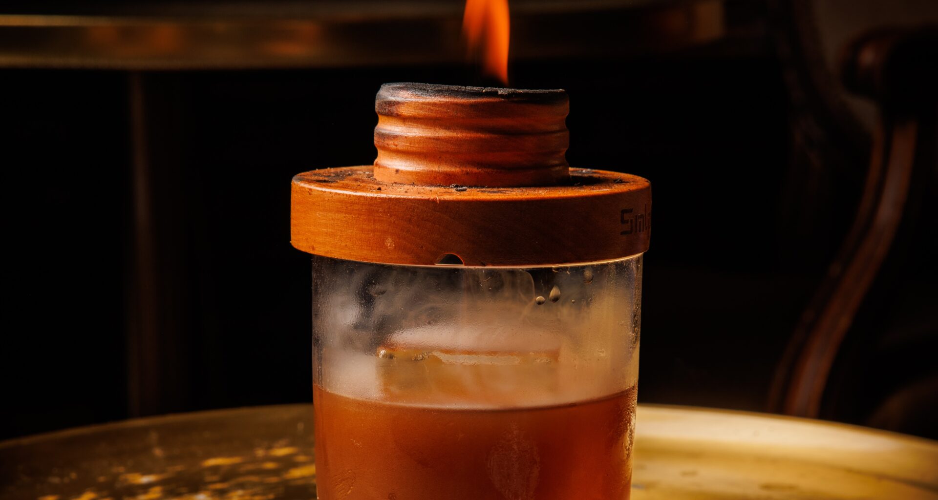 A flame burns atop the lid atop a glass of the opium den cocktail at Apothecary.