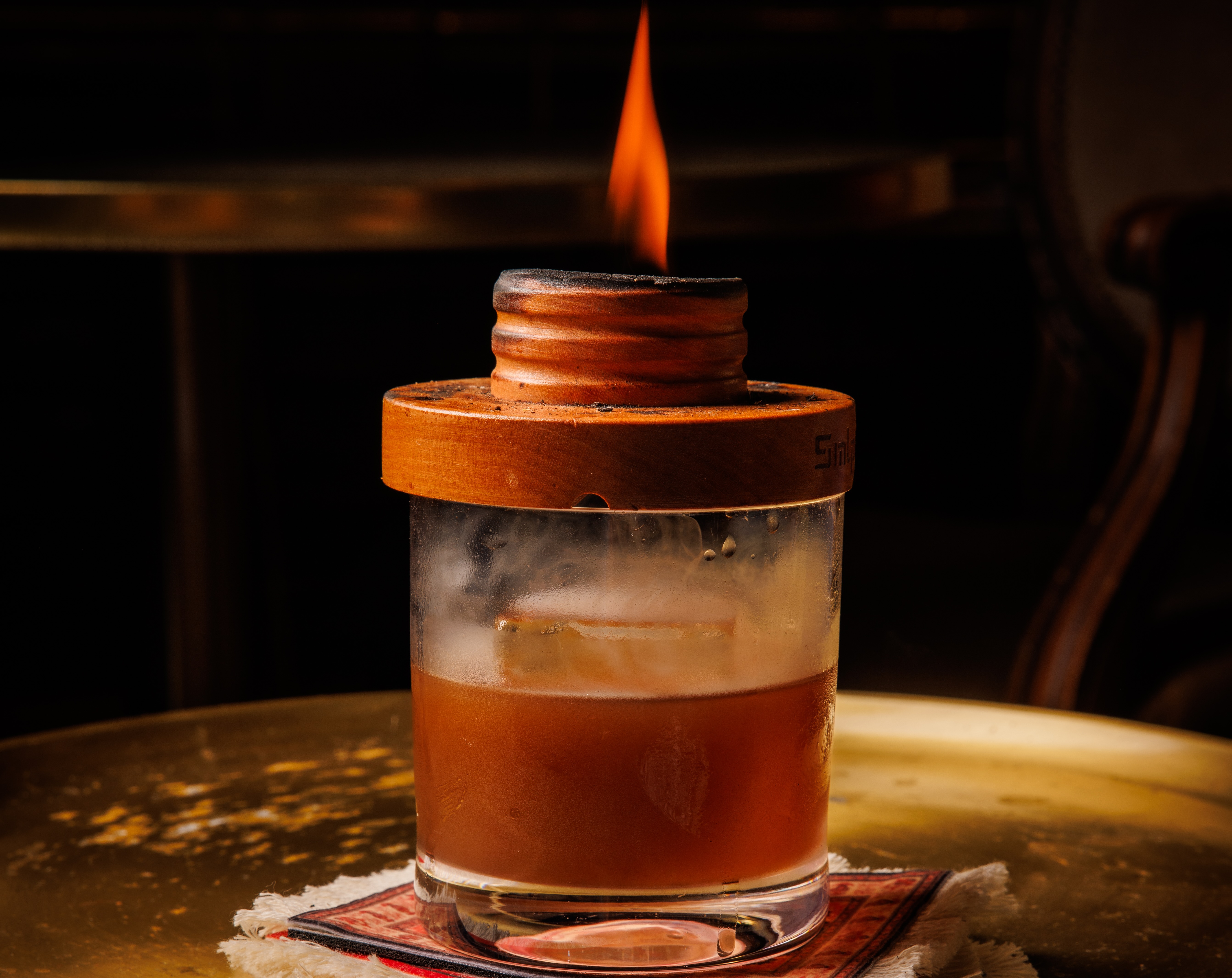 A flame burns atop the lid atop a glass of the opium den cocktail at Apothecary.
