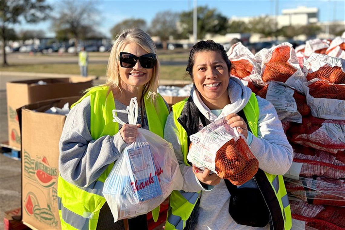Two women holding up bags of donated food at a Tarrant Area Food Bank food distribution event.