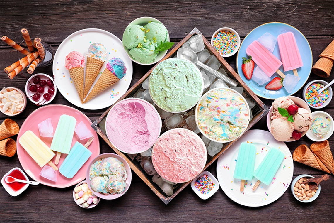 Different ice cream, popsicles and frozen treats. Pastel colors. Overhead view on a dark wood background