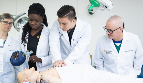 Medical students practice resuscitation techniques on a CPR dummy. A female student on the left pumps a ventilator while a male student on the right does chest compressions.