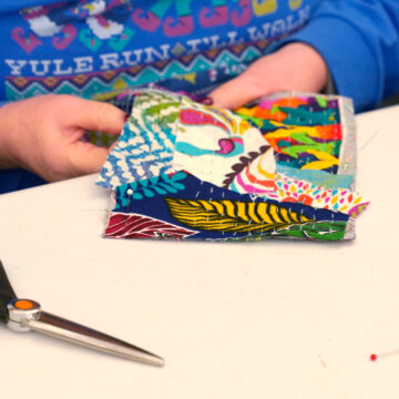 Two hands working on a square of a colorful quilt.