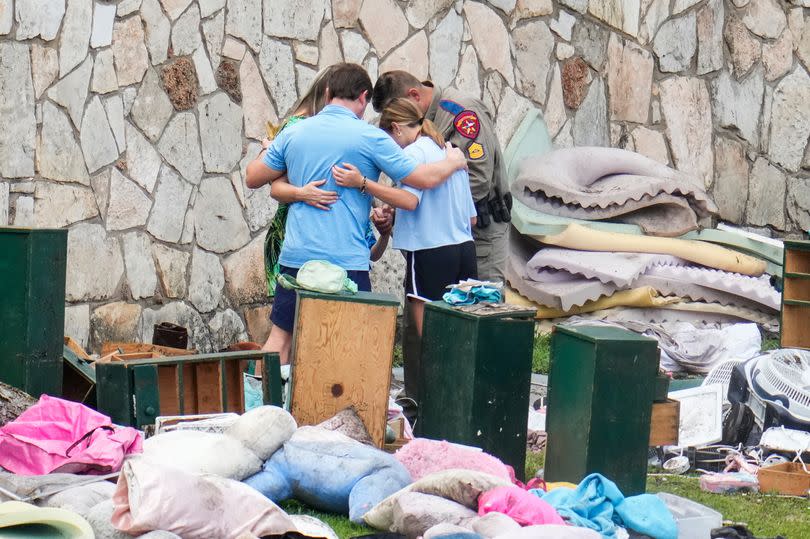 An officer prays with a family as they pick up items at Camp Mystic in Hunt, Texas, July 9, 2025