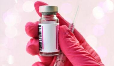 A pink gloved hand holding a vial of medication with a syringe.