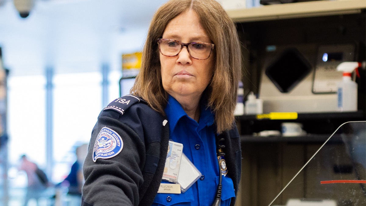A picture of a female TSA workers screening travelers.