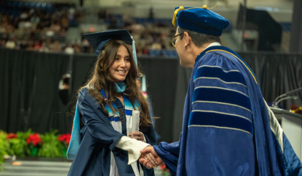 A female graduate shakes hands with a male faculty member after being given her diploma