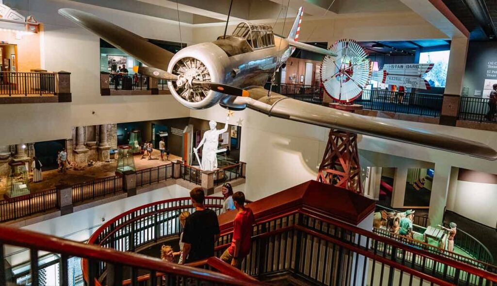 A large gray military airplane suspended from the Bullock Museum gallery ceiling.