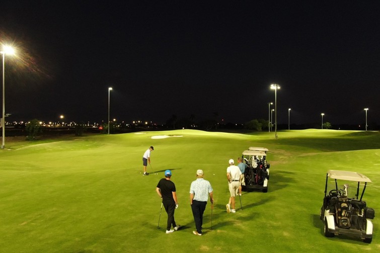 Night scene of five golfers playing The Firefly 9-hole illuminated golf course