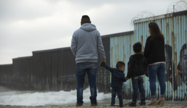 A family stands in front of the USA Mexico border wall.