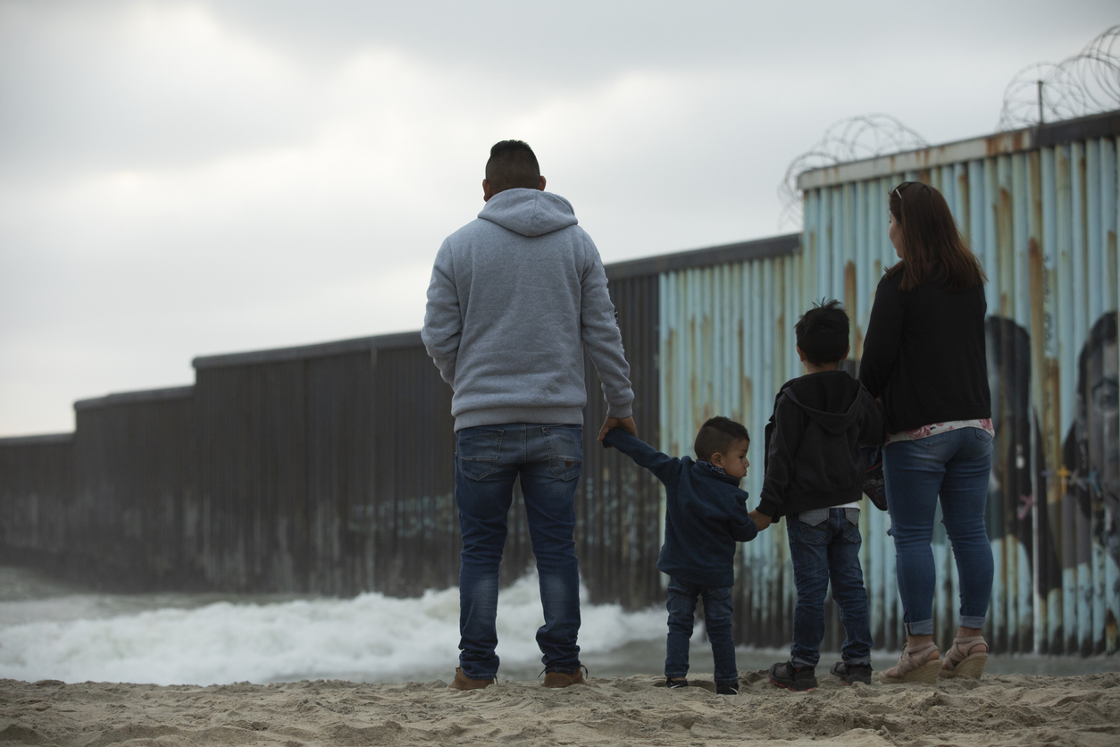 A family stands in front of the USA Mexico border wall.