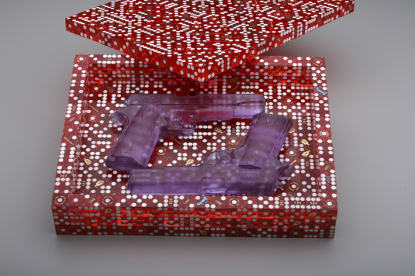 A photograph of a box made from transparent red dominos, opened to reveal a pair of purple transparent guns.