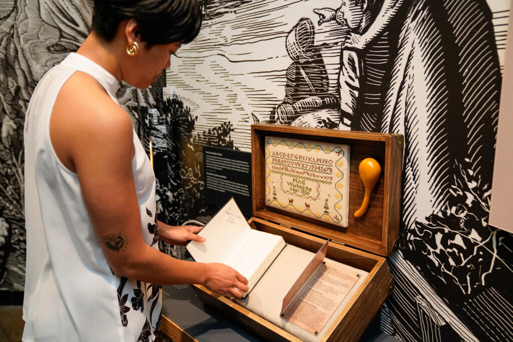 A woman looking at a small open trunk that has a book and other objects in it. 