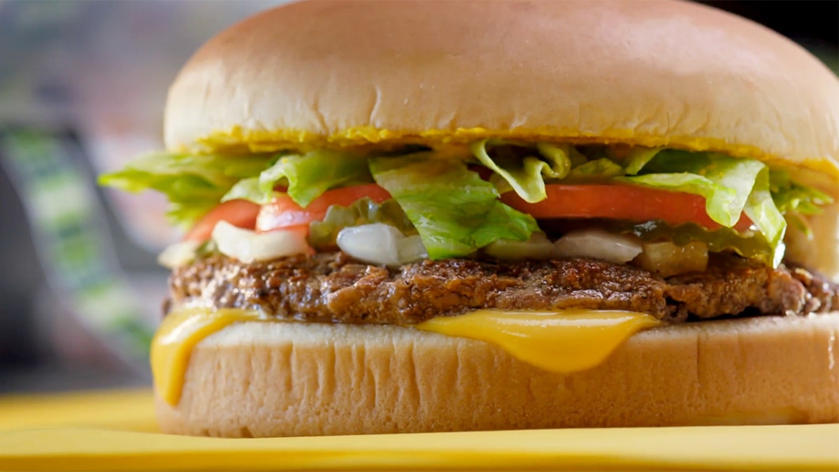 A close-up view of a Whataburger cheeseburger with pickles, onions, lettuce and tomatoes.