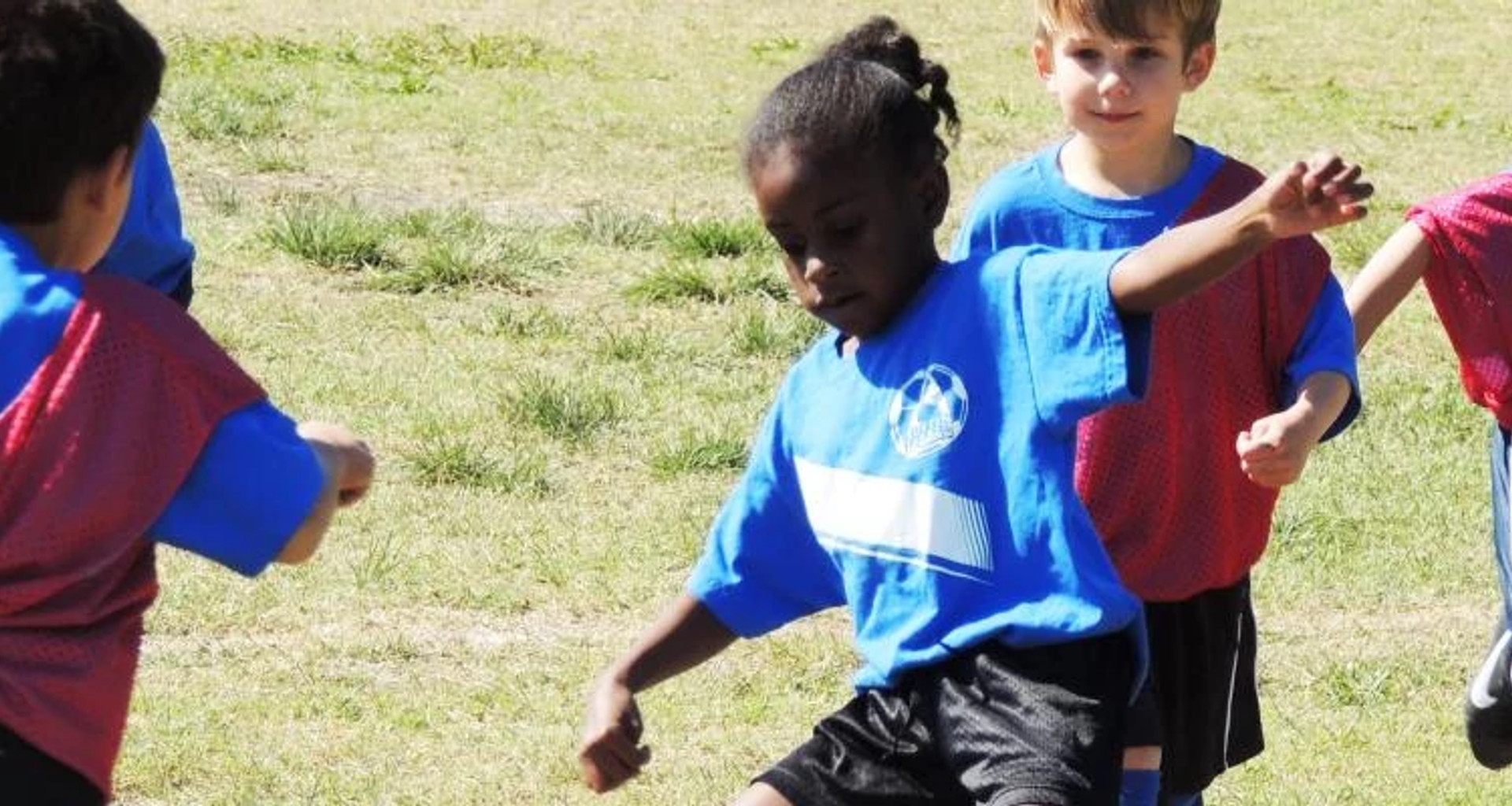 Girl kicking the soccer ball while opposing players come toward her.