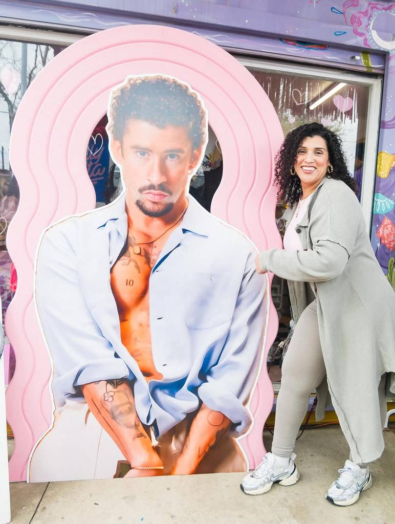 Image shows a fan posing with a blown-up photo of Bad Bunny at a Houston pop-up.
