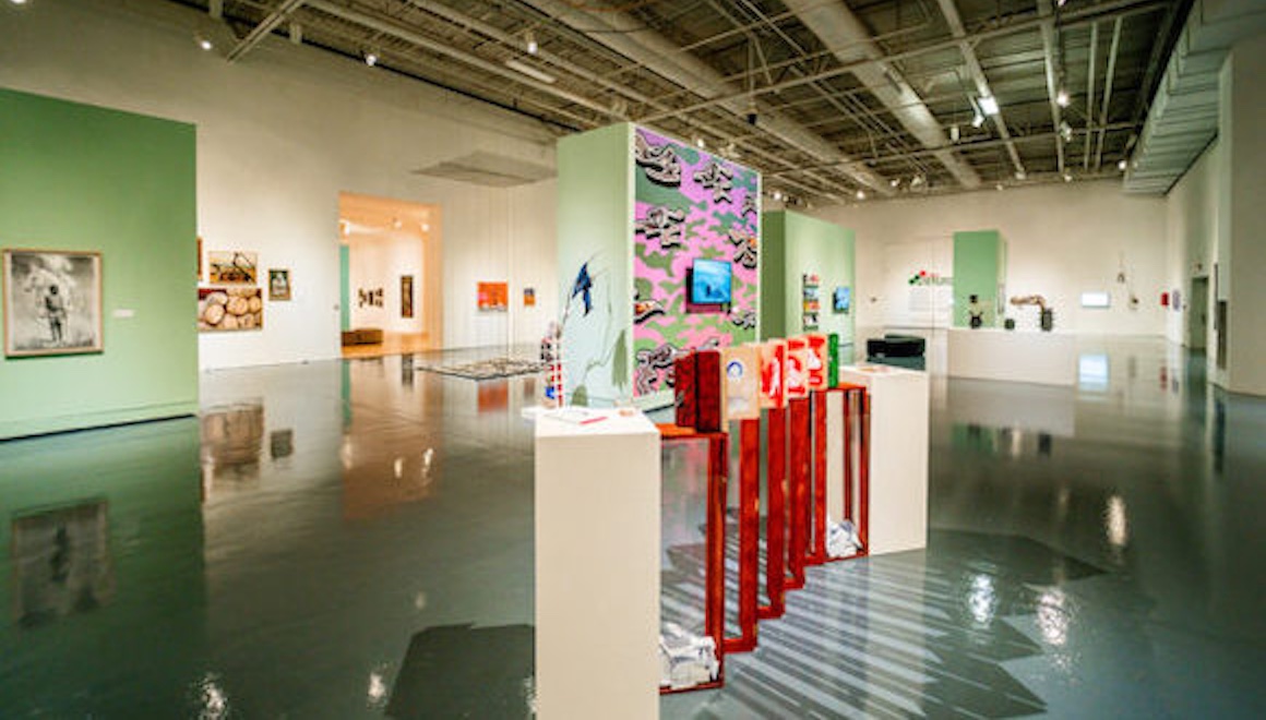 An installation image of the 2024 Border Biennial / Bienal Fronteriza 2024 featuring many artworks on the walls, pedestals and floors.