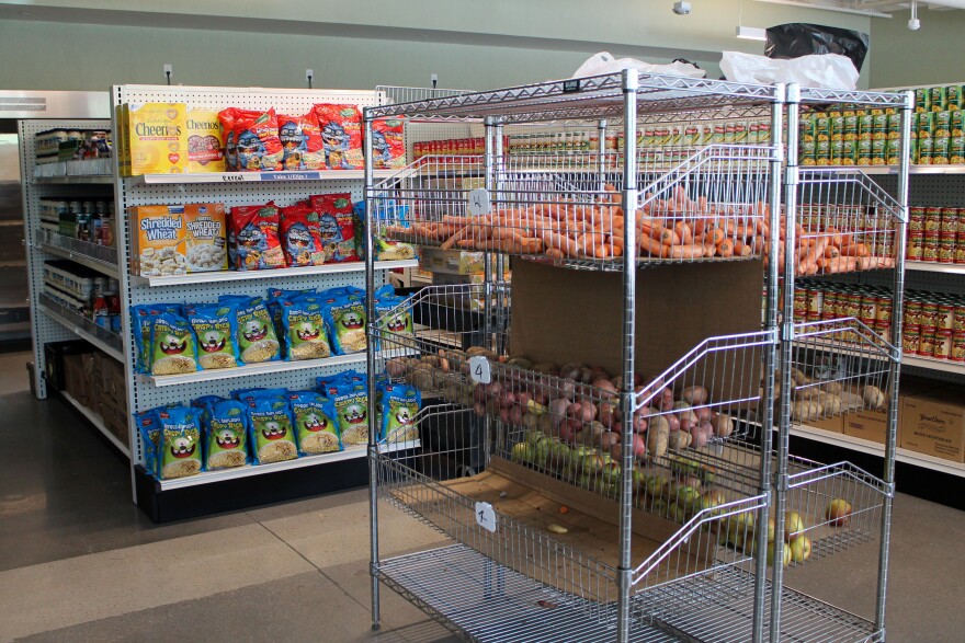 A metal shelf filled with produce sits in from of several small aisles lined with canned and shelf-stable foods.
