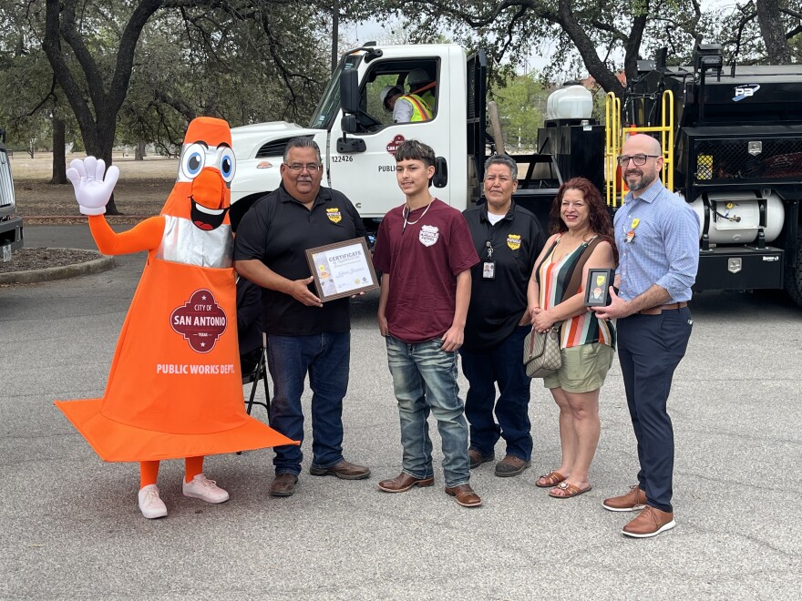 Pothole Patrol mascot Coney and Public Works employees present a certificate to 2026 Fiesta medal artist Adrian Jimenez.