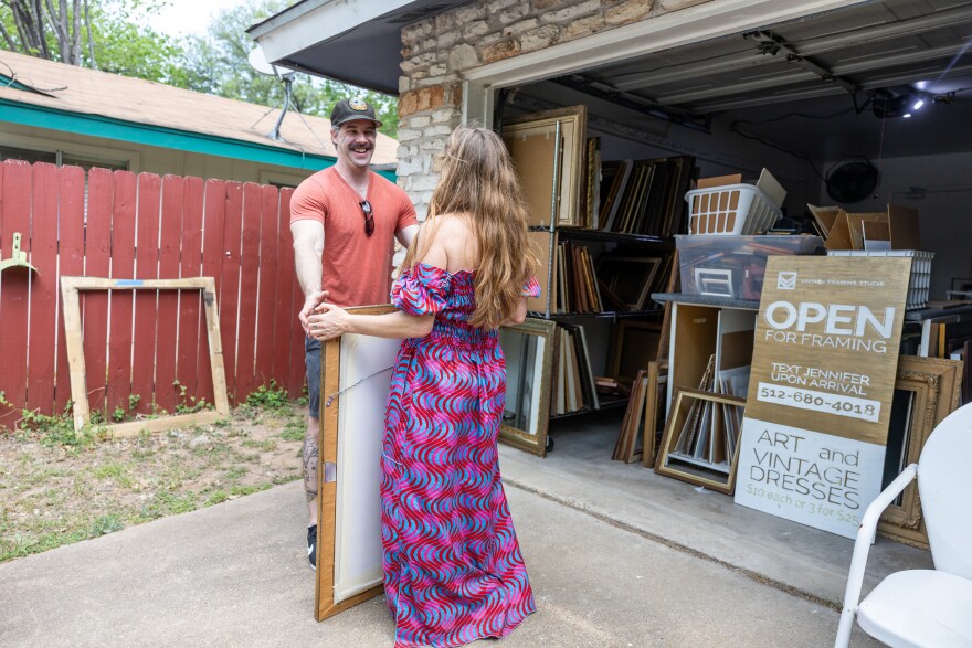 A man stands on one side of a large frame with a woman standing on the other side. They both have their hands on the frame.