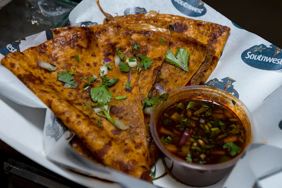 A quesabirria quesadilla with a flour tortilla filled with shredded brisket, melted Monterey Jack cheese, cilantro and diced onions, griddled until golden and served with consommé for dipping, is prepared during a food tasting event for the El Paso Chihuahuas and El Paso Locomotive FC home games at Southwest University Park on Wednesday, Feb. 25, 2026, in El Paso, Texas.