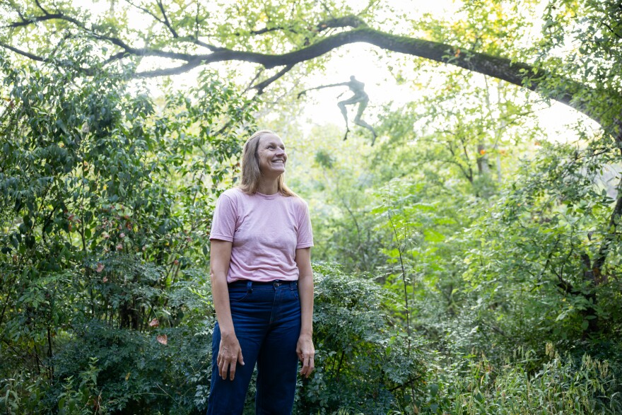 Artist Magdalena Riley, now also an accredited therapist, poses for a portrait in front of her sculpture “Hi Doll” on Friday, August. 22, 2025, along the Barton Creek Greenbelt. Michael Minasi / KUT News