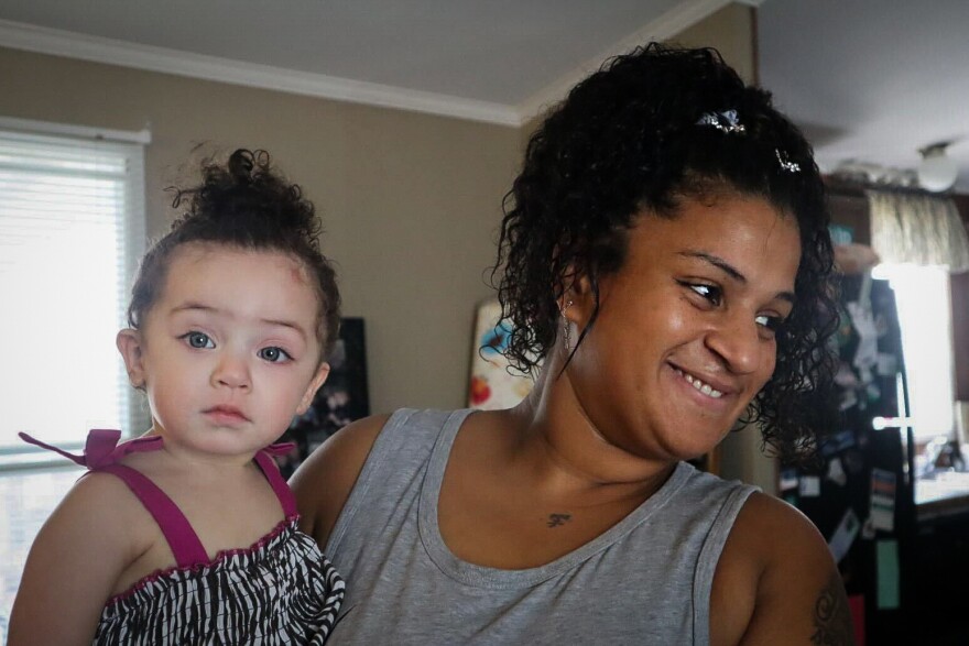 A woman looks at someone out of frame while holding an infant girl, who is looking at the viewer.
