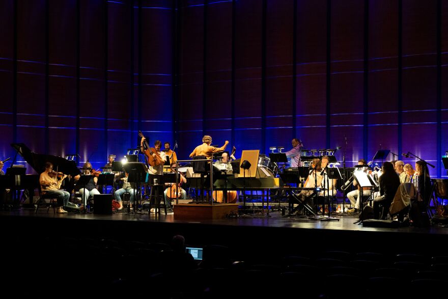 A band plays with the symphony on a stage. 