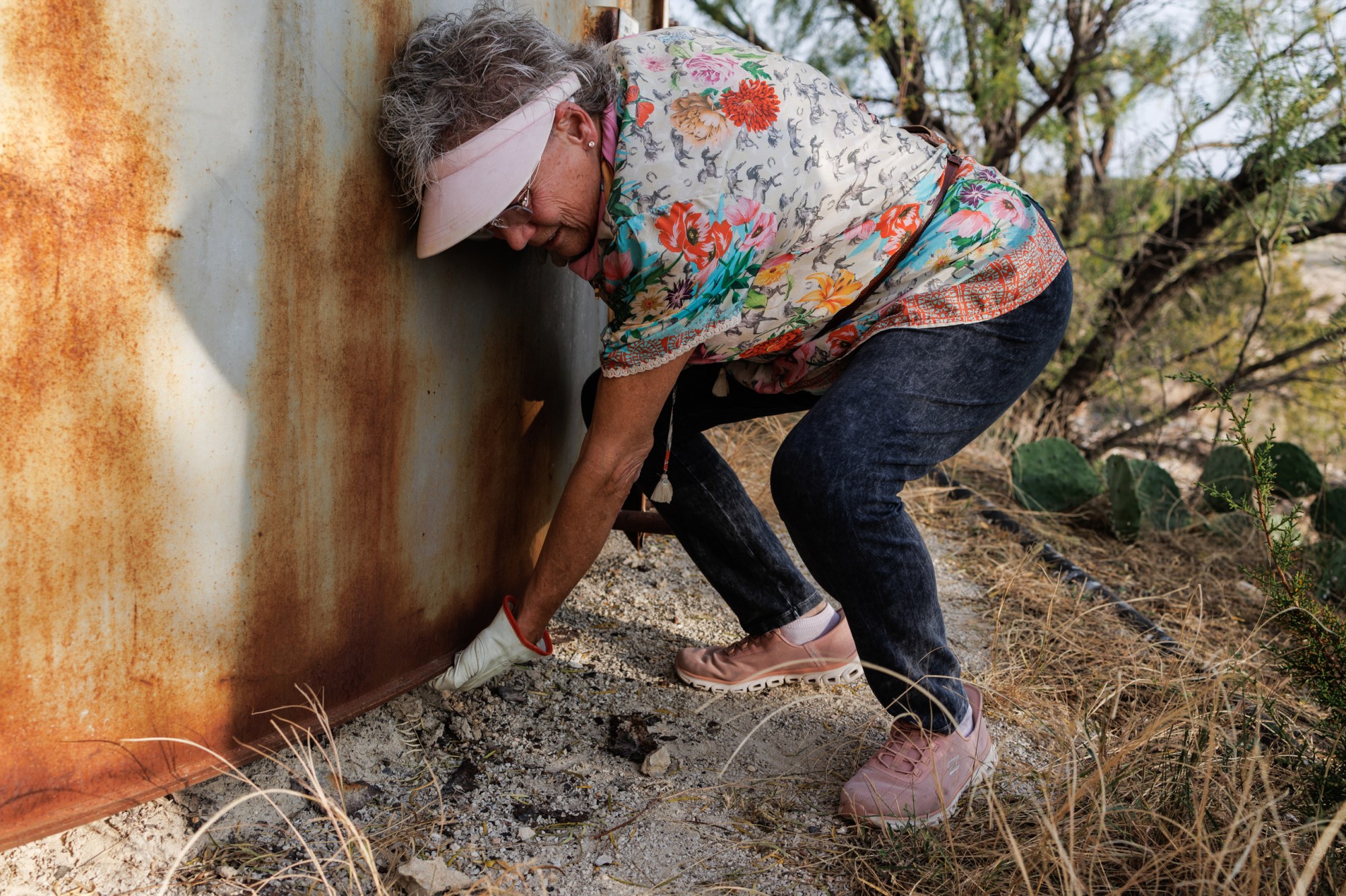 Jackie Lynn Chestnutt feels underneath a tank which is rusted out on its base, part of a tank battery owned by Core Petro LLC which is in disrepair, on her property in Knickerbocker, Texas on Tuesday, November 18, 2025. A large number of orphan oil wells are dotted around her property, causing worry that ground water could be contaminated by leeching oil, produced water or chemicals.