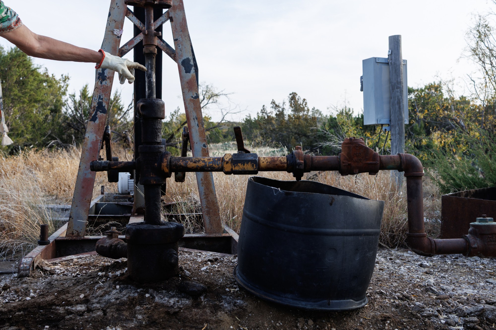 Jackie Lynn Chestnutt points to an oil well owned by Core Petro LLC which is in disrepair and leaking, on her property in Knickerbocker, Texas on Tuesday, November 18, 2025. A large number of orphan oil wells are dotted around her property, causing worry that ground water could be contaminated by leeching oil, produced water or chemicals.