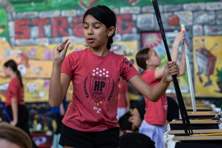 Fifth grader Seva Deshpande makes a gesture with her hand while holding arrows in the other inside the Highland Park Elementary School gym. 