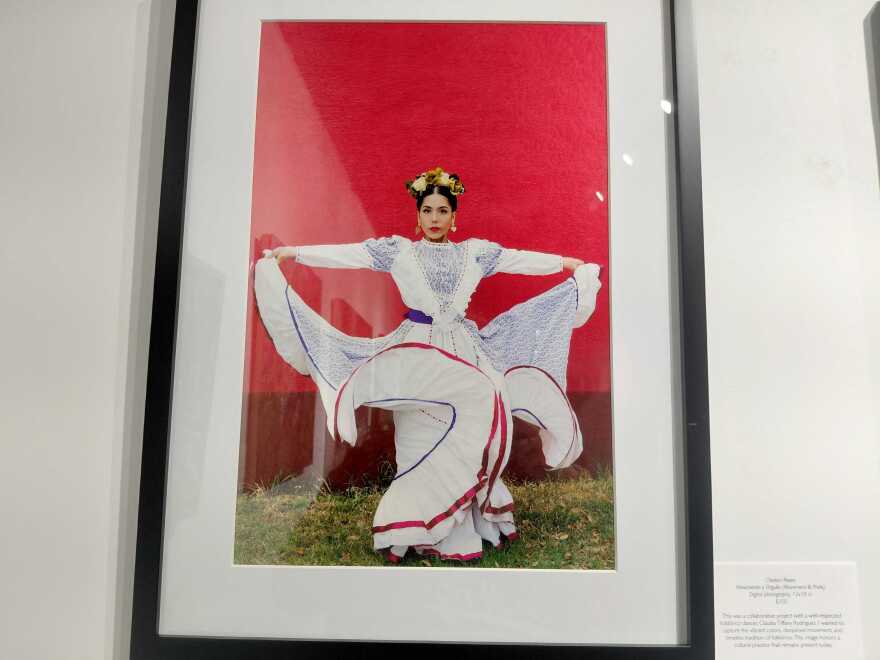 A ballet folklorico dancer stands on the grass wearing a white Jalisco dress with multicolored ribbons. 