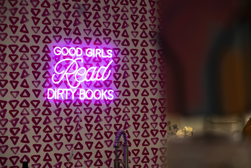 A neon light-up sign that reads "Good Girls Read Dirty Books" hangs on a wall in a romance bookstore in Austin.