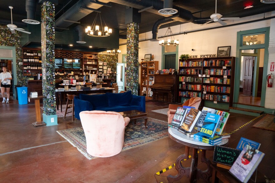 A blue velvet couch in the middle of a room with bookcases full of books and a bar in the back.