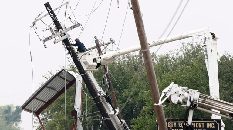 A lineman works to repair a damaged power pole after...