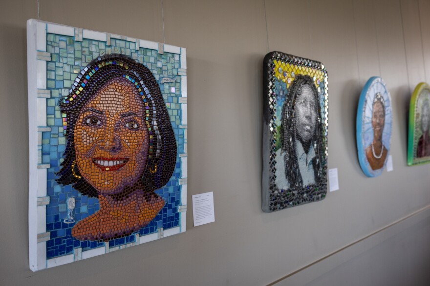 A series of mosaic artworks featuring different people hang on a wall.