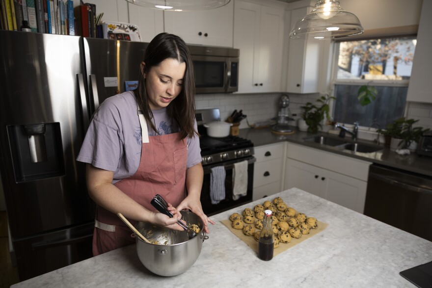 A woman scoops cookie dough out of a bowl to put on a pan at a kitchen island.