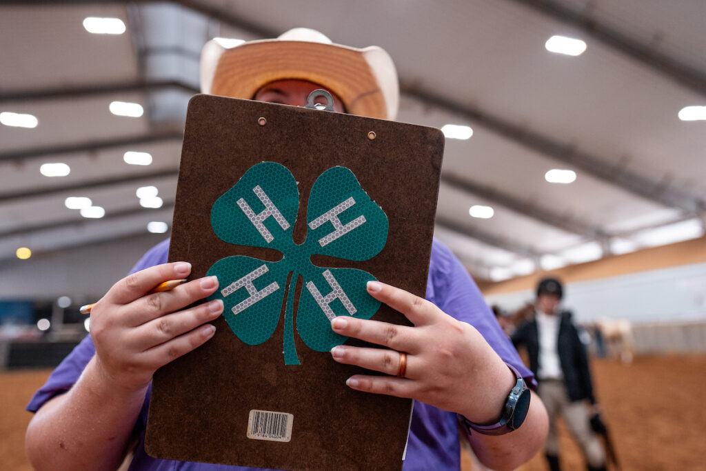 A woman holds a clipboard adorned with a large 4-H four-leafed clover sticker.