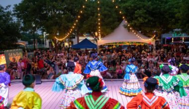 Women in colorful dresses with full skirts look out into a crowd