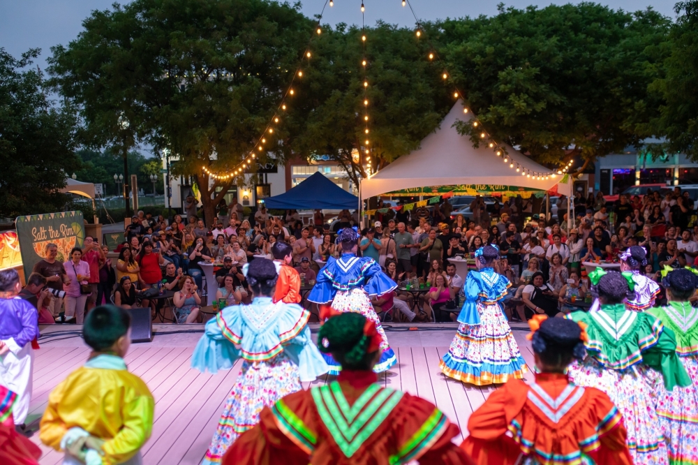 Women in colorful dresses with full skirts look out into a crowd
