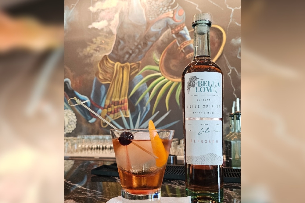 An orange cocktail sits to the left of a bottle of Bella Loma reposado tequila.