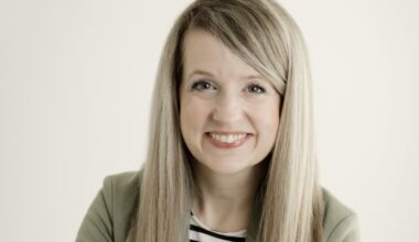 headshot of blonde woman in green jacket with black and white striped shirt