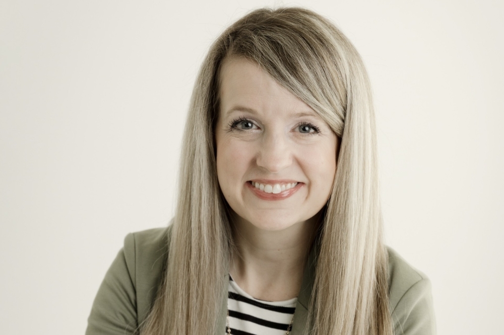headshot of blonde woman in green jacket with black and white striped shirt