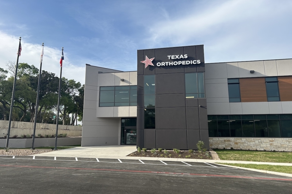 Texas Orthopedics logo with a red star displayed on a two story office building next to flag poles on a sunny day.