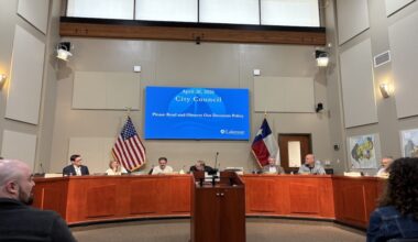 Lakeway City Council chambers with a screen above council members displaying a blue powerpoint.