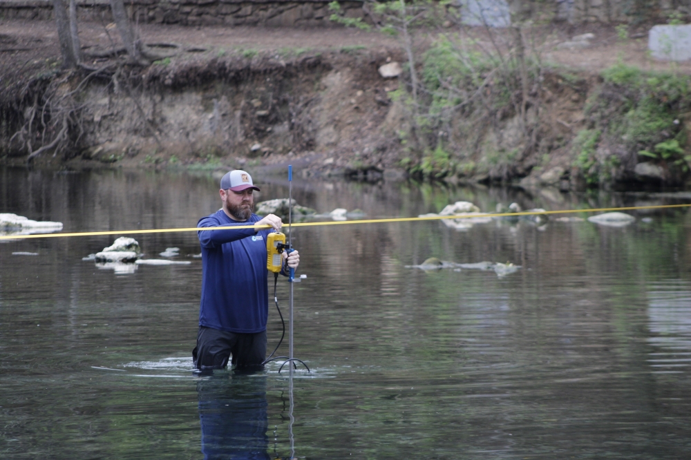 Justin Camp, a Barton Springs-Edwards Aquifer Conservation District hydrogeologist technician, measures flow at Barton Springs. Now in its 45th consecutive month, drought has lowered spring discharge and groundwater levels. (Michael Milliorn/Community Impact)