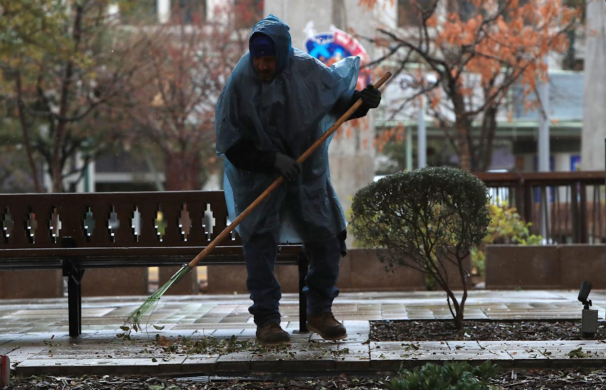 A city employee wearing a rain poncho sweeps leaves at San Jacinto Plaza in El Paso, Texas, on Friday as intermittent rain falls and early‑morning temperatures between 41 and 45 degrees Fahrenheit leave the area feeling sharply colder.