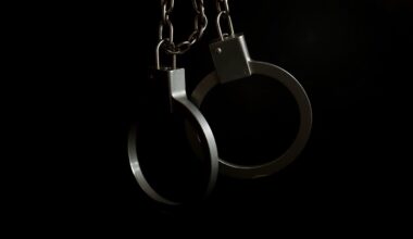 An extreme close-up photograph of metal handcuffs against a dark background, conceptually representing the arrest of a suspect.