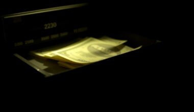 An extreme close-up photograph of a cash register drawer or other crime-related physical evidence object, lit by a harsh, direct camera flash against a pitch-black background, creating a stark, gritty, investigative aesthetic.