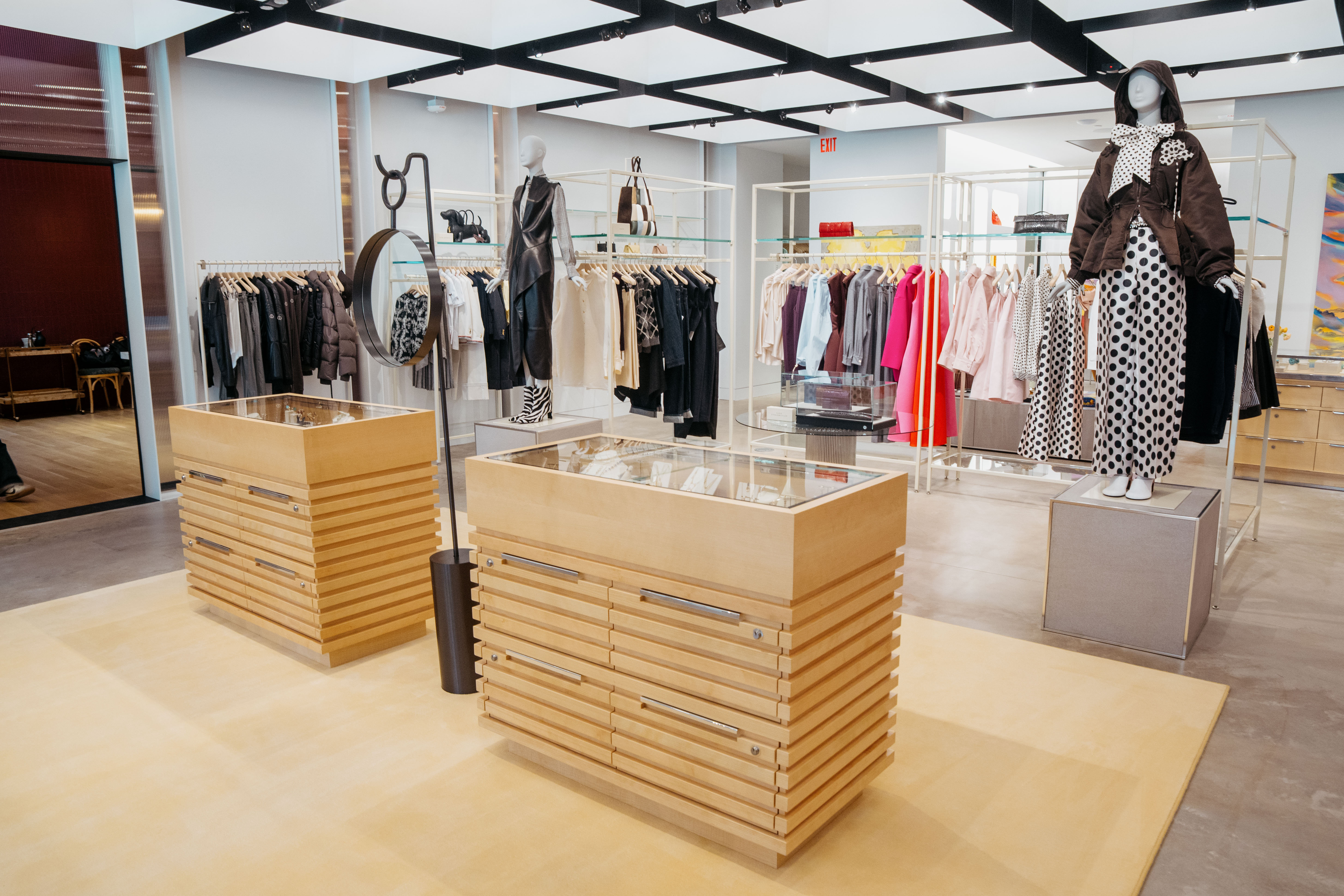 Modern clothing store interior with mannequins, wooden display cases, and racks of various clothes.